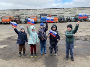 Воспитанники с флагами России на фоне автомобилей 