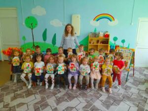 Дети второй младшей группы с воспитателем Матвеевой Е.А. сидят и держат в руках свои рисунки