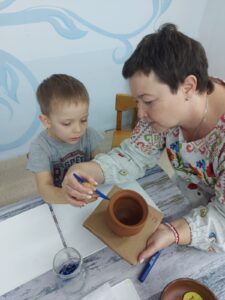 Воспитатель Пивоварова Яна Петровна помогает воспитаннику декорировать готовое из глины изделие